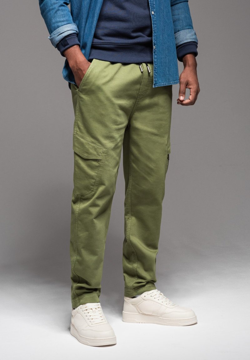 Olijfgroene cargo shorts met zijzakken, een elastische tailleband en een relaxte pasvorm, gecombineerd met witte sneakers en een denim shirt.