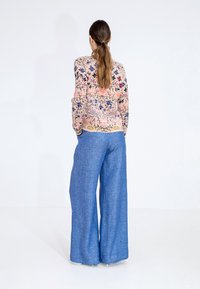 Floral-patterned lightweight knit cardigan in pastel colors, paired with loose-fit, light blue wide-leg trousers in a textured fabric.