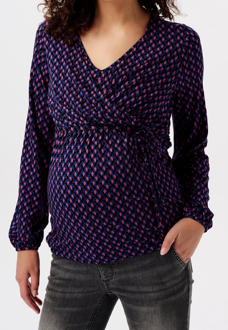 Schwangerschaftsbluse in Marineblau mit rosa und lila geometrischen Mustern. Sie verfügt über ein Wickeldesign, lange Ärmel und eine geraffte Taille mit Bindebändern.