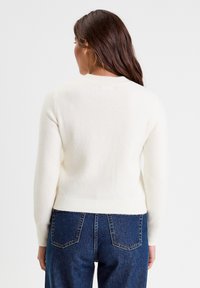 Pull en mélange de laine blanc avec un ourlet et des poignets côtelés, doté d'un col rond et d'une coupe légèrement courte. Assortie avec un jean bleu.