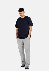 Navy blue cotton t-shirt with short sleeves and a small white logo, paired with light gray pants and black sneakers.