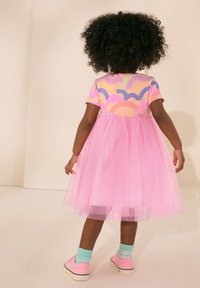 Rosa tyllklänning med en färgglad topp med molnmönster. Korta ärmar, lager-på-lager-kjol och matchas med rosa sneakers och mintgröna strumpor.