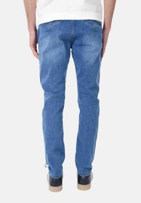 Jeans in denim blu con una vestibilità slim, dotati di due tasche posteriori e leggera scoloritura. Rifiniti con cuciture a contrasto e vita media.