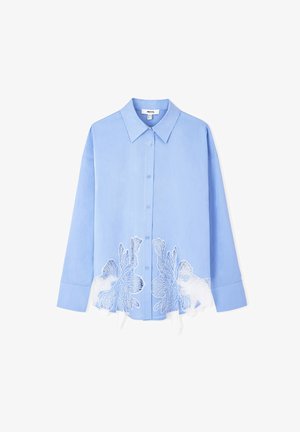 Camisa abotonada de color azul claro con un cuello estructurado y mangas largas, que cuenta con bordados florales blancos en el dobladillo. Textura de tejido suave.