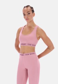 Pink sportmelltartó és hozzáillő leggings emblémázott derékrésszel. Simaszövet, testhezálló fazon, versenystílusú hátkialakítás a fokozott támogatásért.