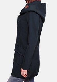 Dunkelblaue, wasserdichte Jacke mit großer Kapuze, Reißverschlussfront, Seitentaschen und einem dezenten Logo-Patch auf der Schulter. Glatte Textur, taillierter Schnitt.