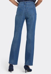 Blå jeans i denim med hög midja, rak passform och bakfickor; kombinerade med mörkblå högklackade skor.