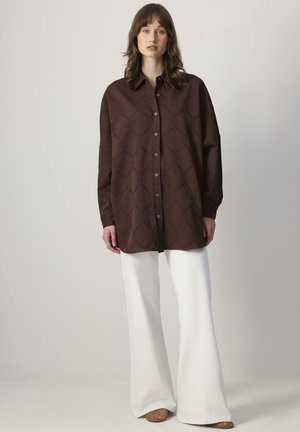 Brown button-up shirt with geometric pattern, long sleeves, and a relaxed fit, paired with white flared pants and woven brown shoes.