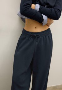 Dunkelblaue Sweatpants mit weitem Bein, elastischem Bund und Kordelzug. Kombiniert mit einem schwarzen Oberteil mit langen Ärmeln und gestreiften Akzenten.
