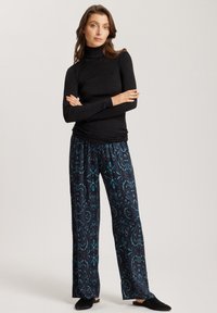 Schwarzes geripptes Rollkragenoberteil kombiniert mit marineblauen, gemusterten, weit geschnittenen Hosen mit türkisfarbenen Blumenmotiven, getragen mit schwarzen Hausschuhen.