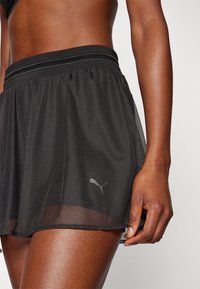 Svart atletisk skort i lätt meshmaterial, med en bred midja och en liten silver Puma-logotyp på fållen.