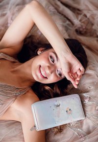 Light pink wallet with a glossy finish, features a whimsical illustration of a character, adorned with silver accents and a zipper closure.