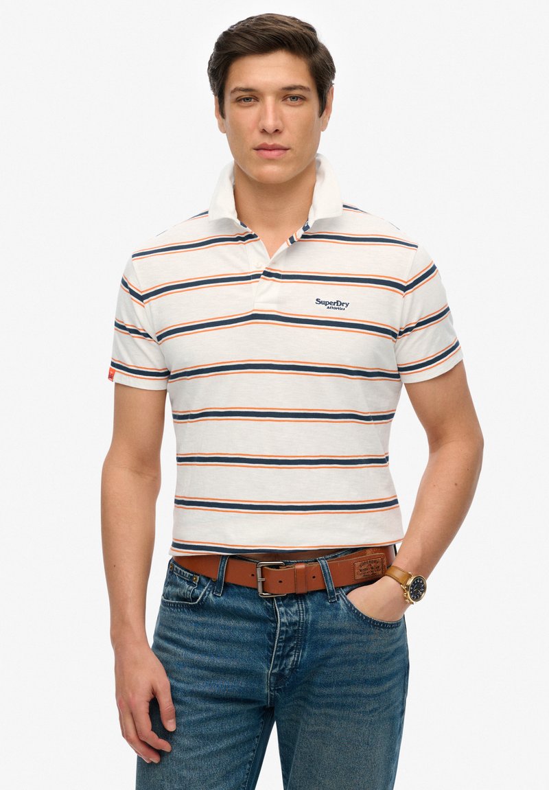 Hvid kortærmet polo t-shirt med marineblå, orange, og røde striber. Har krave, logo på brystet, og bæres med blå jeans og brunt bælte.