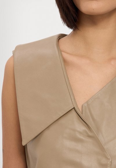 Beige Lederoberteil mit einem strukturierten Kragen und diagonellem Ausschnitt, das eine glatte Textur und klare Linien aufweist.