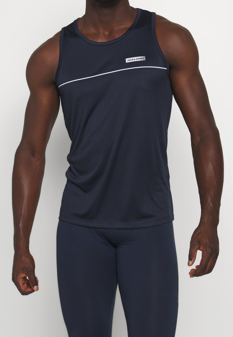 Homme portant un débardeur de sport bleu marine et des leggings ajustés assortis sur fond blanc.