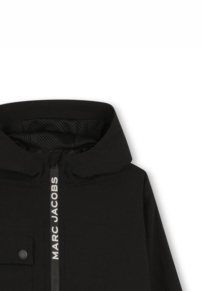 Veste à capuche noire avec tissu texturé, fermeture éclair frontale, doublure en mesh et poche poitrine. Présente le logo "MARC JACOBS" sur la fermeture éclair.