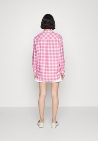 Dlouhý rukáv kostkovaná košile v růžové a bílé barvě, s límečkem na knoflíky a mírně zakřiveným spodním lemem. Měkká tkanina s uvolněným střihem.