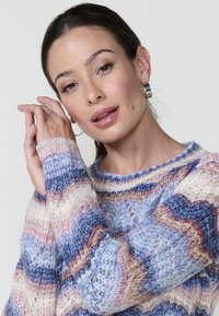Pull en laine avec des vagues multicolores dans des tons de bleu, rose et crème. Il a une coupe ample et de larges manches avec des poignets en côtes.