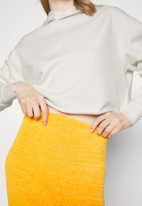 Felpa bianca accorciata con un taglio rilassato, abbinata a una gonna gialla attillata e testurizzata, che mette in risalto il contrasto di colori vivaci.