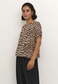 Leopard print top in lightweight fabric, featuring a loose fit, short sleeves, and a rounded neckline. Paired with black, flowy pants.
