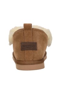 Bruine suede pantoffel met witte bontvoering, platte zool en een achtertab. Beschikt over een gestikt design en een leren label met merk.