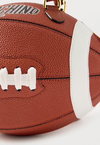 Κοντινή λήψη καφέ δερμάτινης αμερικανικής μπάλας ποδοσφαίρου με λευκά κορδόνια, λευκή ρίγα, μαύρα ραφές και χρυσό μεταλλικό δαχτυλίδι προσαρτημένο.