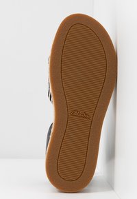 Semelle de chaussure avec une bande de roulement en caoutchouc brun clair, arborant le logo Clarks au centre, présentée sur un fond blanc.