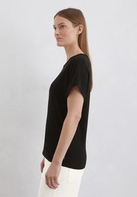 Svart kortärmad topp i mjukt tyg, med avslappnad passform och rund halsringning. Stylen matchas med ljusa byxor.