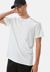 T-shirt sportivo bianco realizzato in tessuto leggero e liscio. Caratterizzato da maniche corte, scollo a girocollo e sottili dettagli grigi sulle spalle.