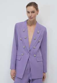 Blazer lavanda con scollatura a V profonda e decorazioni floreali argentate. Forma sartoriale, due tasche frontali e tessuto leggero e testurizzato.