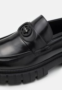 Mustad musta nahast loafer, millel on sile viimistlus, silmapaistva musta logo tüübliga ja paks tekstuuriga tald.