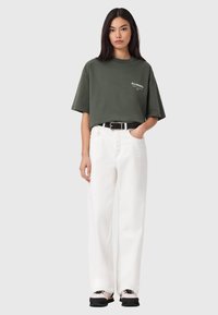 Vihreä ylisuurikokoinen t-paita valkoisella logolla, yhdistetty valkoisiin korkeavyötäröisiin housuihin ja mustaan vyöhön. Päällä mustat ja kermaiset lenkkarit.