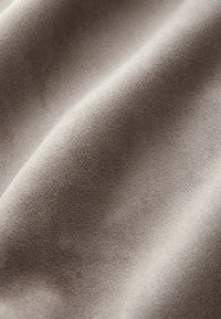 Lichtbeige stof met een zachte, gladde textuur, die fijne geweven patronen en een subtiele glans toont in een gedrapeerde positie.