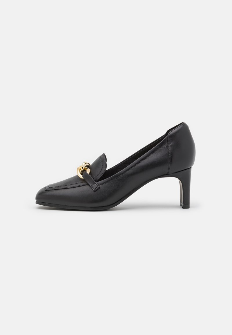 Mocassin en cuir noir à talon moyen, bout pointu avec détail chaîne dorée sur le dessus, montré de profil sur fond blanc.