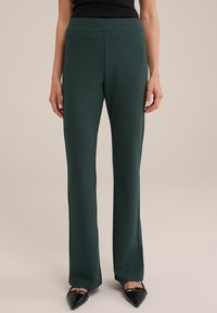 Žalios, aukštu liemeniu kelnės su tiesiu kirpimu, pagamintos iš elastingos medžiagos. Turi lygią tekstūrą ir nematomus akcentus.