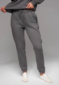 Graue Jogginghose mit elastischem Bund, Zugbanddetails und gerippten Bündchen. Aus weichem Stoff gefertigt, mit einem kleinen Logo an der Seite.