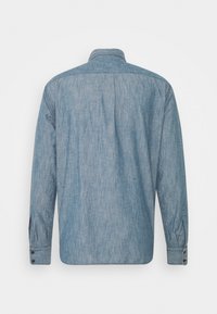 Dlouhý rukáv, světle modrá džínová košile s knoflíkovými manžetami zobrazená zezadu na bílém pozadí.