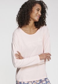 Light pink long-sleeve top with a wide neckline and white text reading "Sleep solves everything." Soft fabric and relaxed fit.
