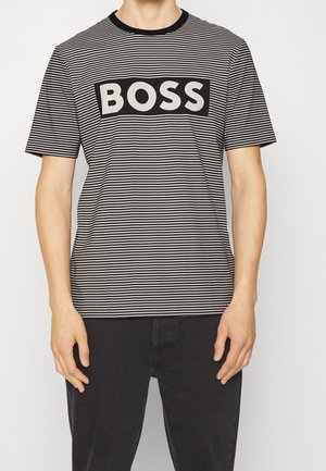Mand iført en sort- og hvid- vandret striped T-shirt med ordet "BOSS" i fed hvide bogstaver på en sort rektangulær baggrund.