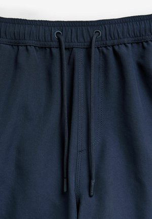 Navy modri šortki z vrvico za prilagajanje v pasu, elastičnim pasom in gladko teksturo tkanine. Imajo kontrastno šivanje in plastične konice.