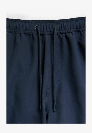 Tumesinine lühikesed püksid, millel on nööriga vöökoht, elastne riba ja sile kangast tekstuur. Omab kontrastset õmblust ja plastikust aglet-otsasid.