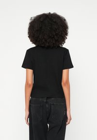 T-shirt preta de manga curta com decote redondo. Feita de tecido liso, ligeiramente ajustada com um comprimento médio. Combinada com jeans escuros.