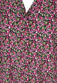 Blouse florale avec un fond sombre, ornée de fleurs roses et vertes, fermeture par bouton et une texture de tissu qui semble douce et légère.