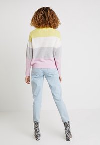 Pull color-block en jaune, gris, blanc et rose ; coupe ample avec poignets et ourlet côtelés ; associé à un jean bleu clair et des bottes imprimé serpent.