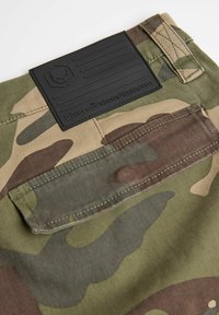 Spodnie cargo w kamuflażu w zielono-brązowym kolorze. Posiadają czarną gumową metkę z logo, kieszeń z tyłu oraz wzmocnione szwy.