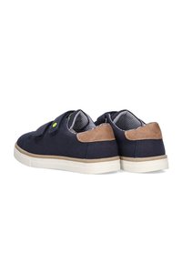 Zapatos de lona azul marino con detalles en ante marrón, dos correas de Velcro, suela de goma blanca y forro interior a rayas. Se muestra vista trasera.