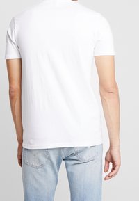 Bílý krátký rukáv tričko, bavlněný materiál, kulatý výstřih, hladká textilie, jednoduchý design, s světle modrými džíny a viditelným švem na zadní straně.
