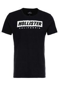 Černé bavlněné tričko s krátkým rukávem. Má bílý blokový logo s textem "HOLLISTER" a "CALIFORNIA" v tučném písmu, umístěný na střední části předního dílu.