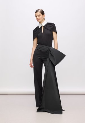 Black top with a white collar features a keyhole opening and cape sleeves; matching black wide-leg pants with a large bow accent at the waist.