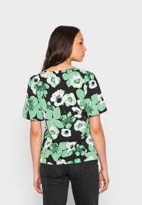 Top preto de manga curta com um padrão floral que apresenta grandes flores brancas e verdes. Tecido suave com um corte descontraído e decote redondo.